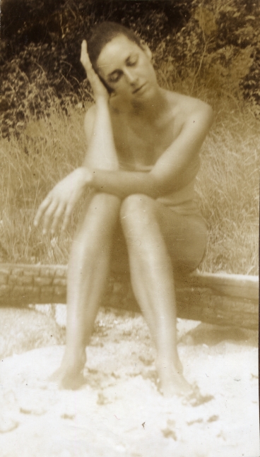 Woman in a bathing suit sitting on a fallen tree trunk on the beach resting her head in her left hand
