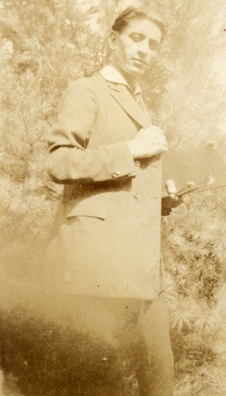 Faded sepia photograph of a young man in a suit holding a palette and two paint brushes